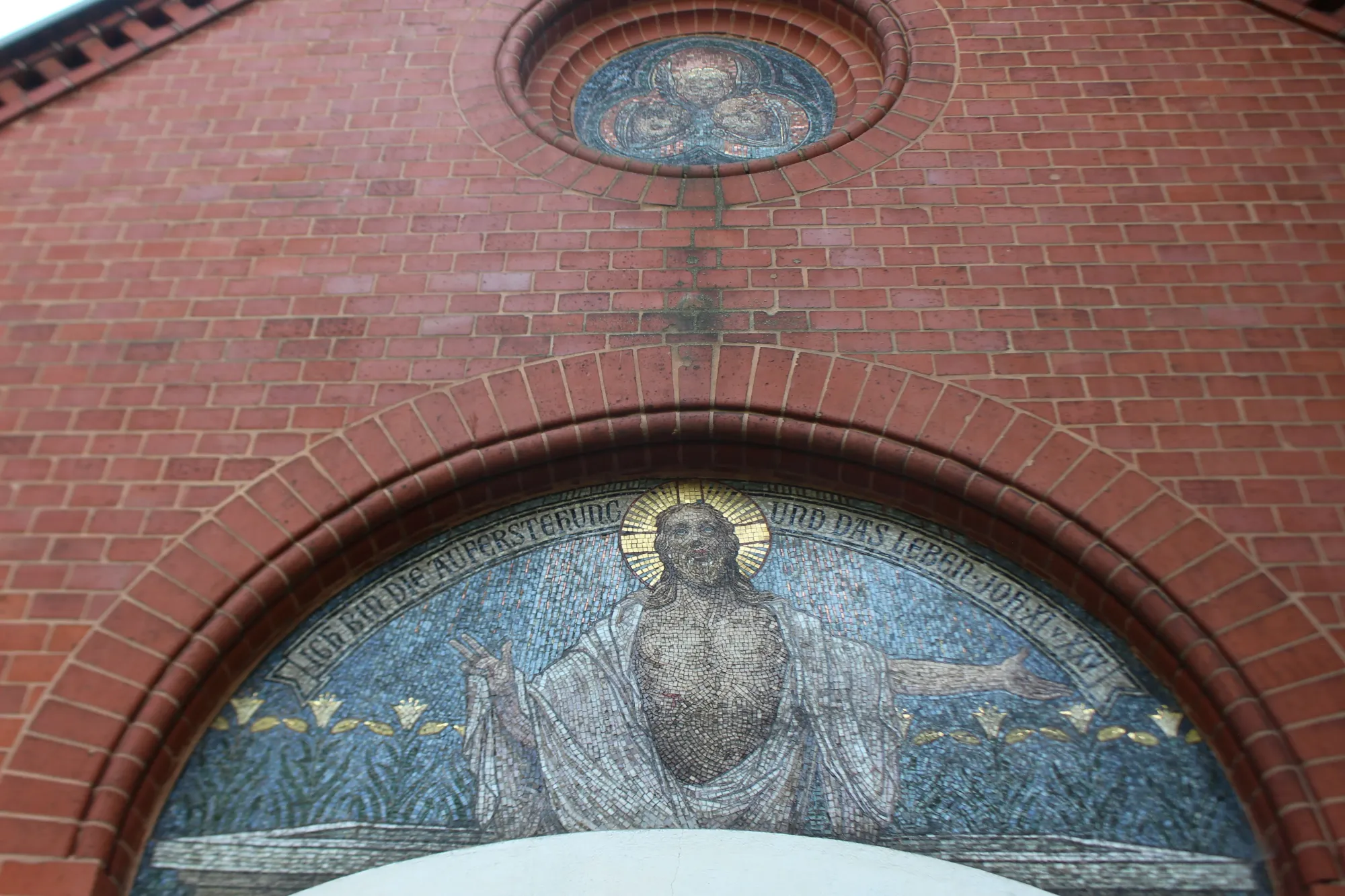 Mosaik über dem Eingang der Kapelle: Christus mit ausgebreiteten Armen in einem Rundbogen aus Backstein